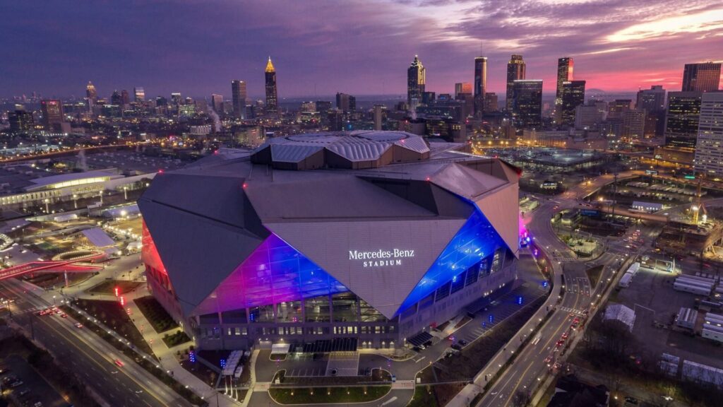 Mercedes-Benz Stadium lit up at dusk with the downtown Atlanta skyline behind it
