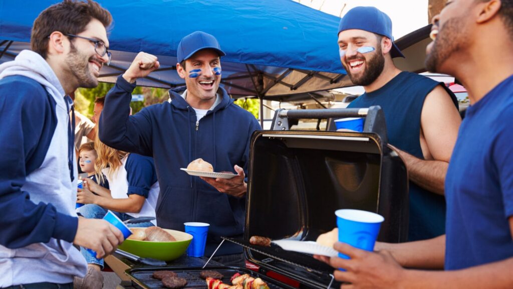 Football fans tailgating under a tent around a grill